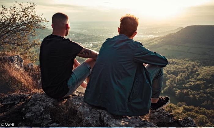 Zwei junge Männer sitzen auf einem Felsen und schauen ins Tal