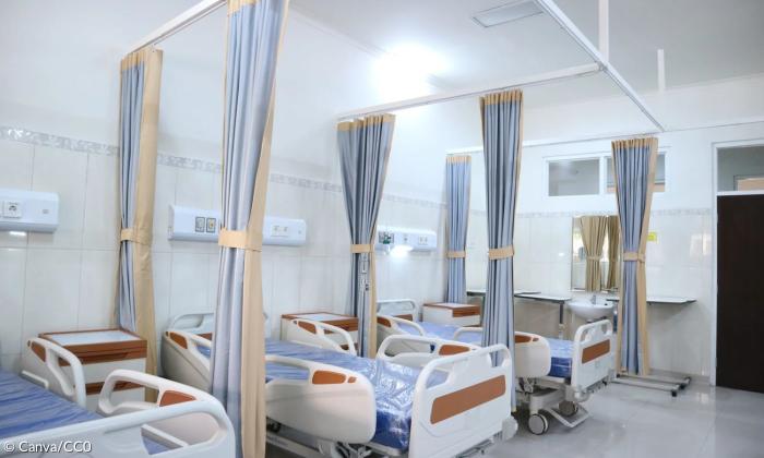 Man sieht das in helles Licht getauchte Zimmer einer Klinik. Es stehen drei betten auf der einen Seite, die jeweils von nicht zugezogenen Vorhängen umgeben sind. 