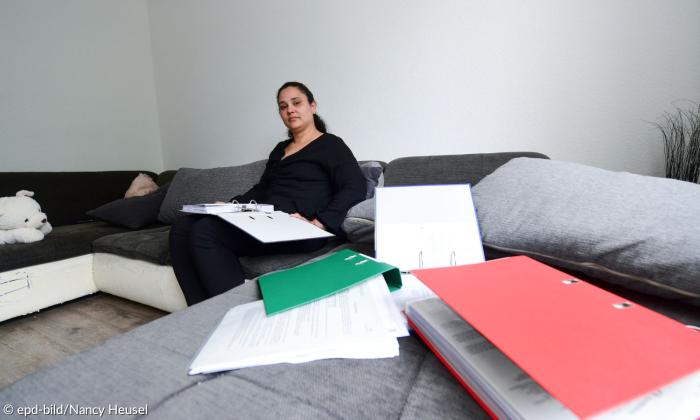 Eine Frau auf einem Sofa, davor Aktenordner und Papiere