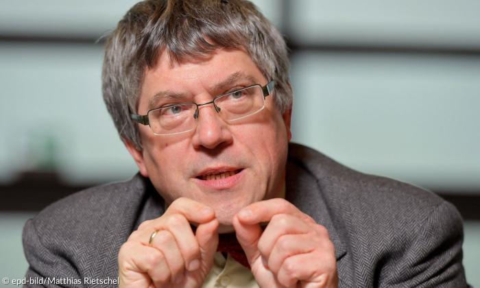 Porträtaufnahme eines Mannes, der knapp an der Kamera vorbei blickt. Er trägt eine Brille sowie einen grauen Anzug. 