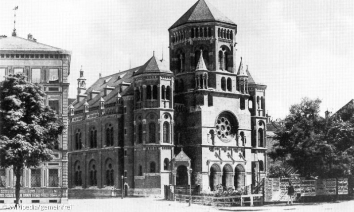 Auf dem Schwarz-Weiß-Bild erkennt man einen Flügel sowie die Front einer großen Synagoge. Links neben ihr bahnt sich ein weiteres großes Haus an. 