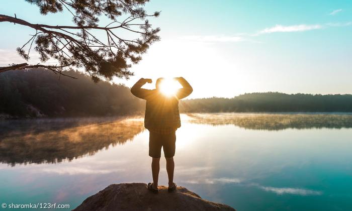 Ein Mensch steht vor einem Sonnenaufgang am Wasser