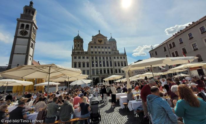 Mehrere Hundert Menschen feiern auf dem Rathausplatz in Augsburg bei strahlendem Sonnenschein an der großen Friedenstafel zusammen das Friedensfest.