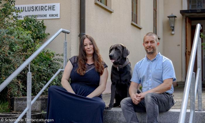Zwei Menschen und ein Hund vor einer Kirche