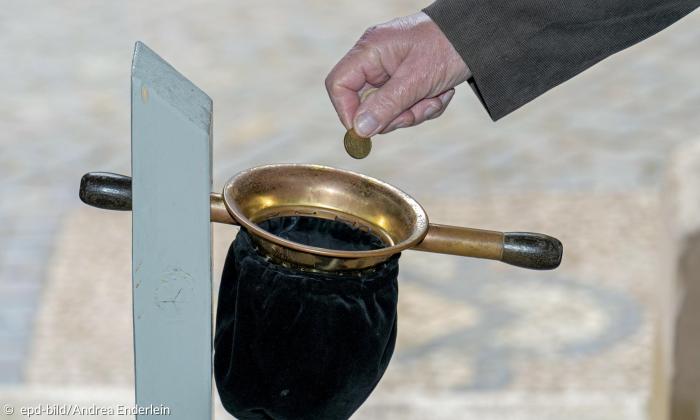 Die Hand einer  älteren Person wirft eine Münze in einen Klingelbeutel