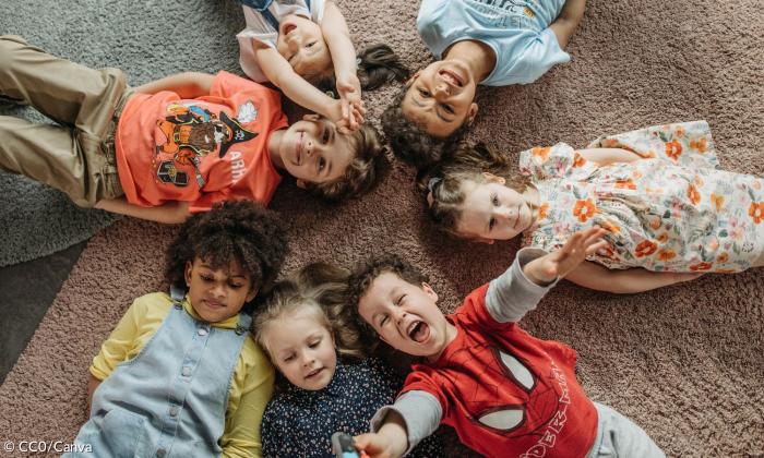 Gruppe von Kindern liegt auf einem Teppich und freut sich. 