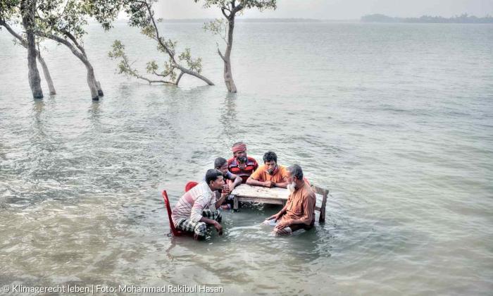 Fünf dunkelhäutige Menschen sitzen im Wasser an einem Tisch