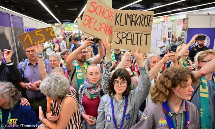 Menschen halten Schilder hoch, auf denen "Schöpfung bewahren" und "Klimakrise spaltet" steht