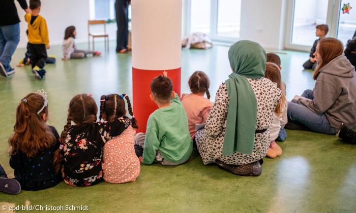 Kinder und Erzieherinnen sitzen auf dem Boden