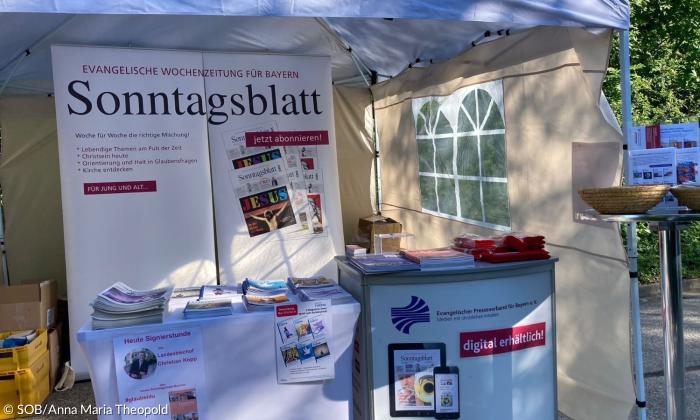 Ein Stand, mit Plakaten, auf denen Sonntagsblatt steht
