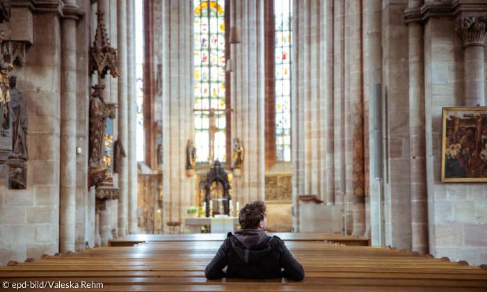 Von hinten abgebildeter Mann sitzt in einer Kirche