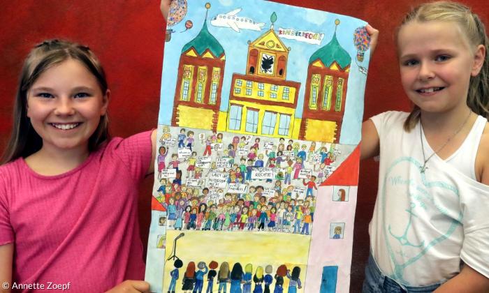 Zwei Mädchen halten ein Bild, auf dem Kinder mit Plakaten zu sehen sind
