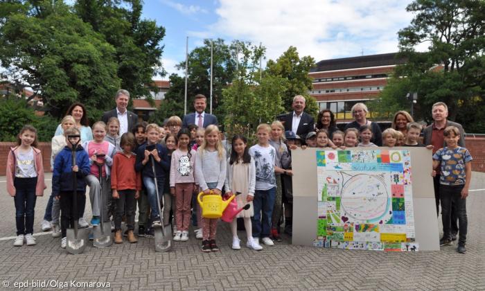 Viele Kinder und einige Erwachsene stehen nebeneinander und halten ein buntes Plakat