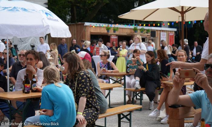 Menschen sitzen auf Bierbänken und unter Sonnenschirmen