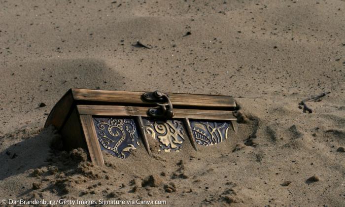 Eine Schatzkiste mit goldenen Beschlägen ragt aus Sand hervor
