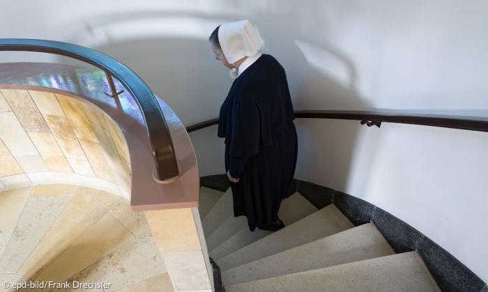Eine Frau mit weißer Haube und schwarzem Gewand im Treppenhaus
