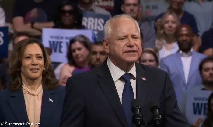 Ein Mann im Anzug, dahinter eine Frau im Blazer, dahinter viele Menschen mit Schildern
