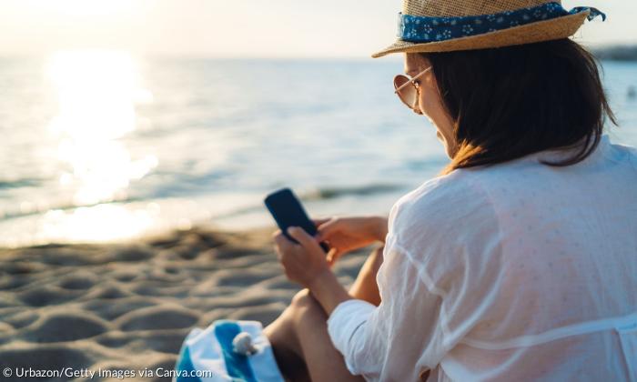 Eine Frau sitzt am Strand und schaut auf ihr Handy