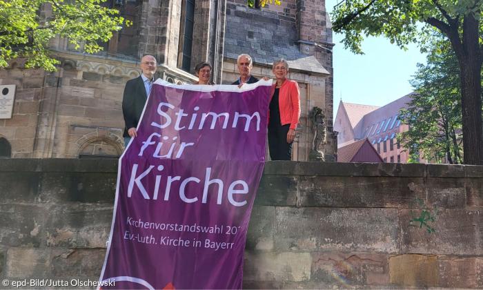 Bernhard Petry, Britta Müller, Jörg sichelstiel, Berthild Sachs mit dem Banner zu den Kirchenvorstandswahlen 2024 vor der Nürnberger Kirche St. Sebald. 