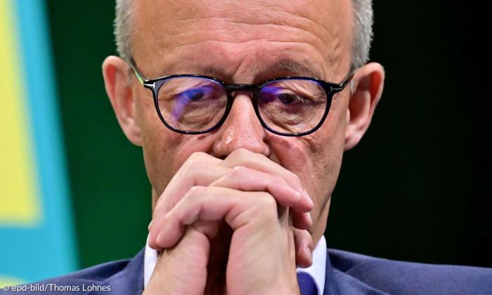 Ein Mann mit Brille faltet die Hände vor dem Mund