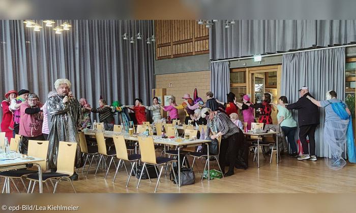 Menschen in bunten Kostümen ziehen in einer Polonaise durch einen Raum