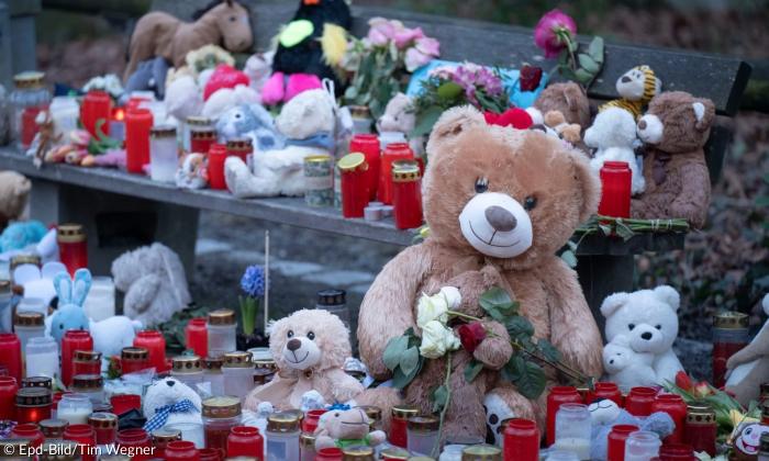 Blumen, Kerzen und ein Teddybär liegen auf dem Boden 
