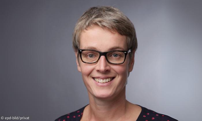 Eine Frau mit kurzen Haaren und Brille lächelt