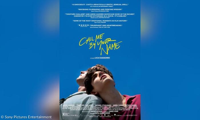 Es ist ein Filmplakat mit der Aufschrift "Call me by your Name". Man sieht den Himmel als tiefblauen Hintergrund und im Vordergrund sind zwei Männer, die sich aneinander lehnen und in die Ferne blicken.
