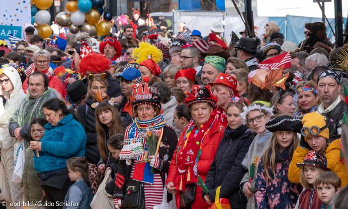 Viele verkleidete Menschen stehen in einer Gruppe und gucken zur gleichen Seite. Sie warten auf den Faschingszug.