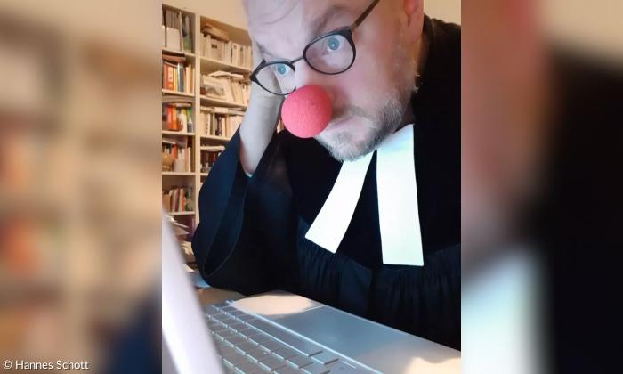 Ein Mann mit roter Clownsnase und Pfarrer-Gewand