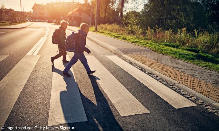 Kinder gehen mit Schulranzen über eine Straße