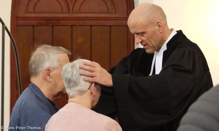 Ein Pfarrer legt seine Hände segnend auf die Köpfe von Gottesdienstbesucherinnen
