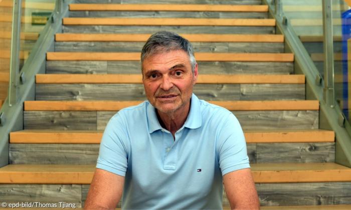 Ein Mann im hellblauen Polohemd sitzt auf einer Treppe