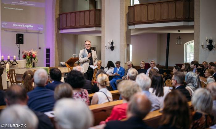Ein Mann steht in einer Kirche mit einem Mikro in der Hand