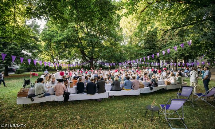 Menschen sitzen an weißgedeckten Tischen im Freien