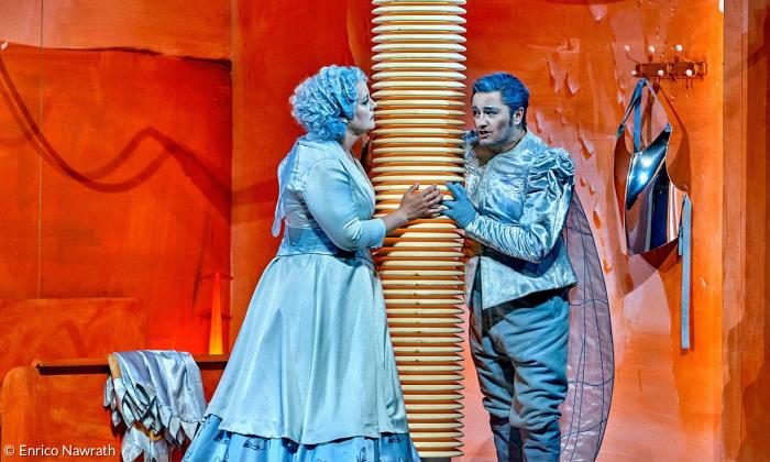 Eine Frau und ein Mann in blauen Gewändern vor einer orangen Wand
