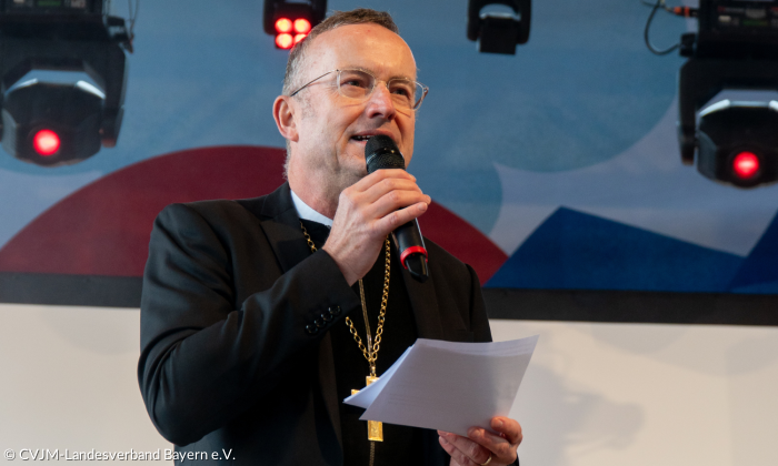 Landesbischof Christian Kopp predigt auf der Bühne mit Mikrofon in der einer und Zettel in der anderen Hand.