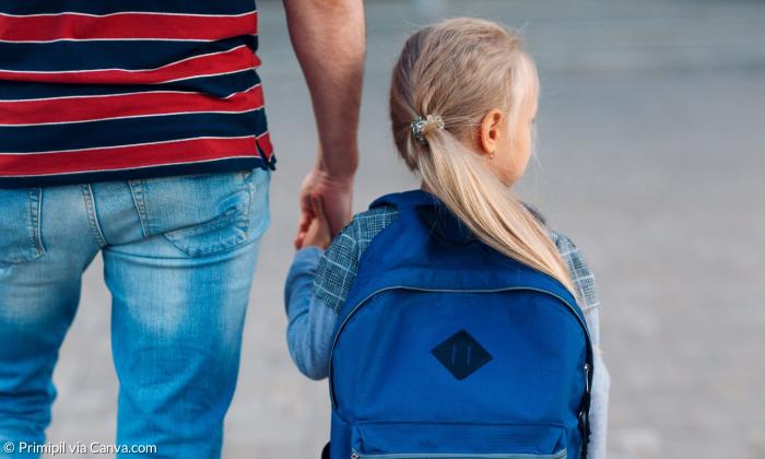 Ein kleines Mädchen mit Rucksack an der Hand eines Mannes