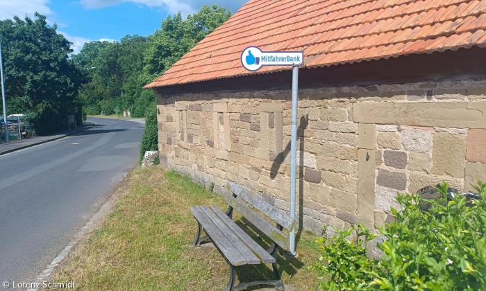 Eine Bank, an der ein Schild mit der Aufschrift "Mitfahrerbank" steht