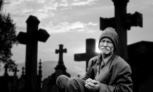 Ein Mann sitzt vor einem Grab im Friedhof