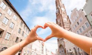 Hände bilden ein Herz vor dem Kirchturm der Landshuter Stadtpfarrkirche.