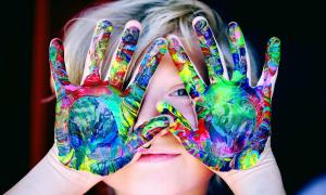 Kind hält Hand mit Farbe vor das Gesicht