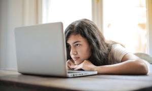 Eine junge Frau schaut auf ihren Laptop-Bildschirm, ihr Gesichtsausdruck ist eher missbilligend