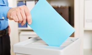 Ein blauer Zettel wird in eine Wahlurne gesteckt