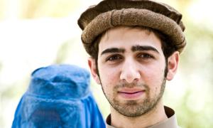 Ein junger afghanischer Mann, im Hintergrund eine Frau mit Burka