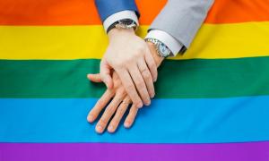 Zwei Männerhände vor einer Regenbogenfahne