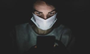 Eine Frau mit einer Maske, die auf einen Handybildschirm blickt.