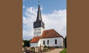 Die Kirche in Weisendorf. Davor ist ein Friedhof, der Himmel ist blau.