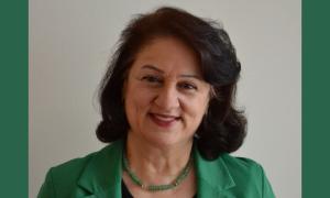 Porträt von Mitra Sharifi Neystanak. Sie hat schwarze Haare, lächelt in die Kamera und trägt eine grüne Anzugsjacke sowie eine grüne Kette.