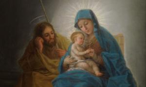 Maria hält das Jesuskind im Arm. Josef sitzt neben ihr. Beide schauen auf das Kind.